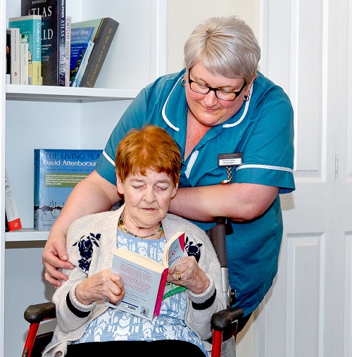 Elderly resident with dementia reading with carer